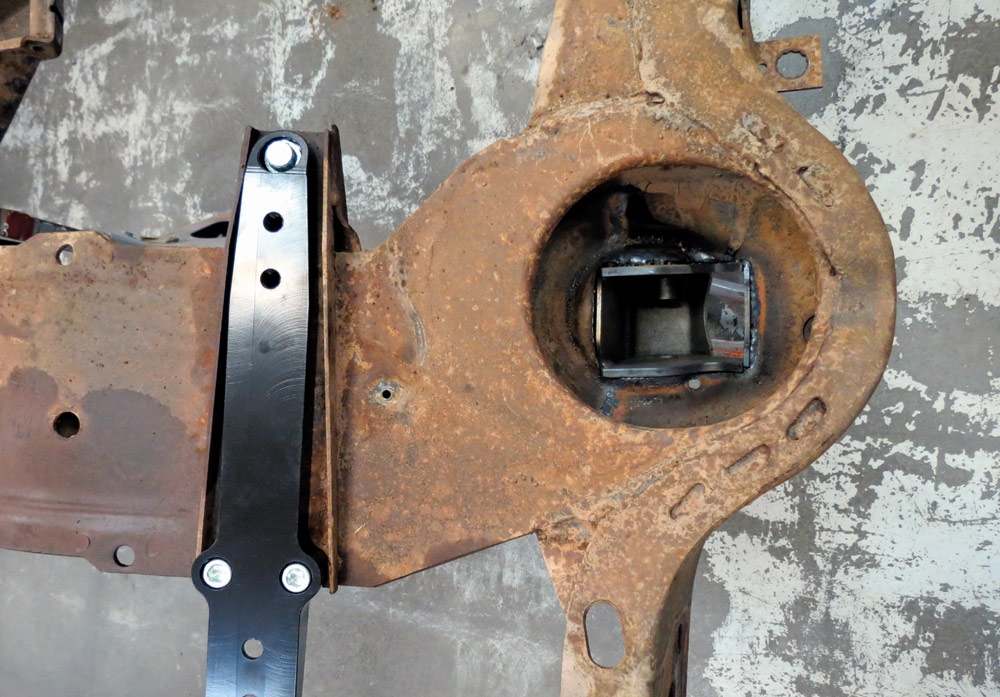 A top-down view showing a black alignment tool bolted across the rusted frame rail next to a newly welded-in suspension pocket to ensure perfect structural geometry.