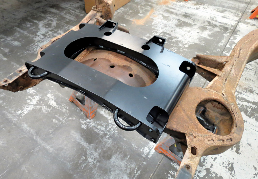 A newly painted black steel crossmember is placed onto the rusted chassis for a final mock-up, illustrating the structural upgrades being added to the vintage frame.
