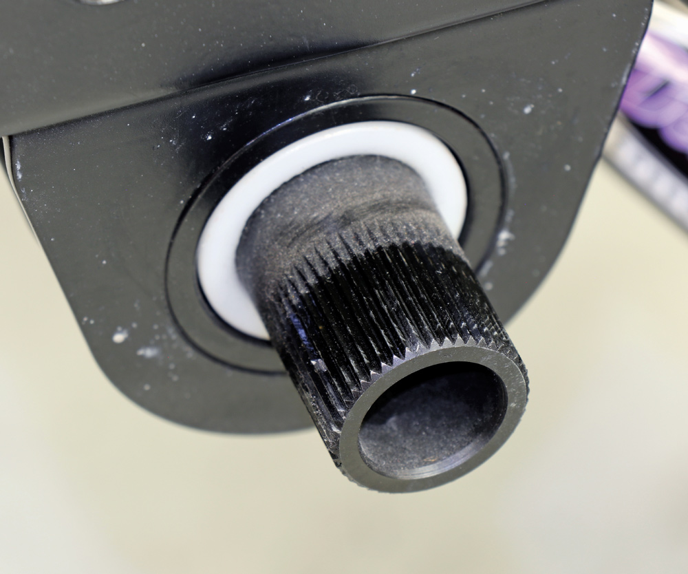 Extreme close-up of a splined black sway bar end emerging through a white low-friction bushing inside the black powder-coated chassis mounting bracket.