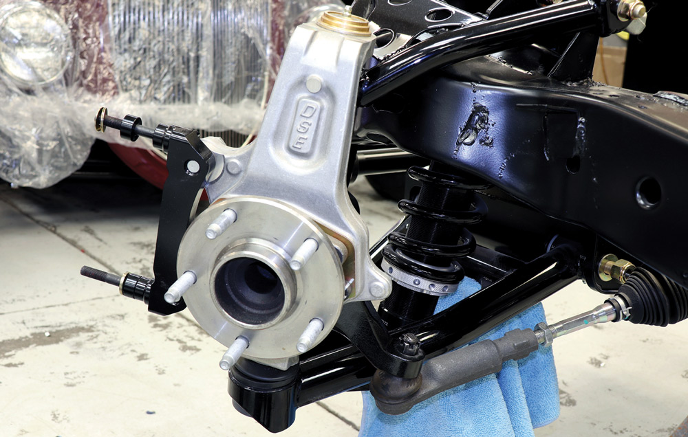 Front suspension detail showing the installed aluminum spindle, wheel hub with studs, and the mounting bracket for a high-performance disc brake system.