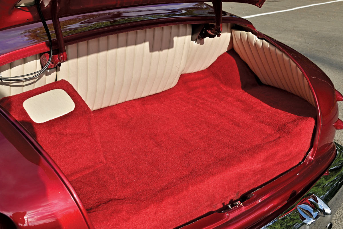 The fully upholstered trunk of the custom Mercury, featuring plush red carpeting and off-white pleated vinyl panels.