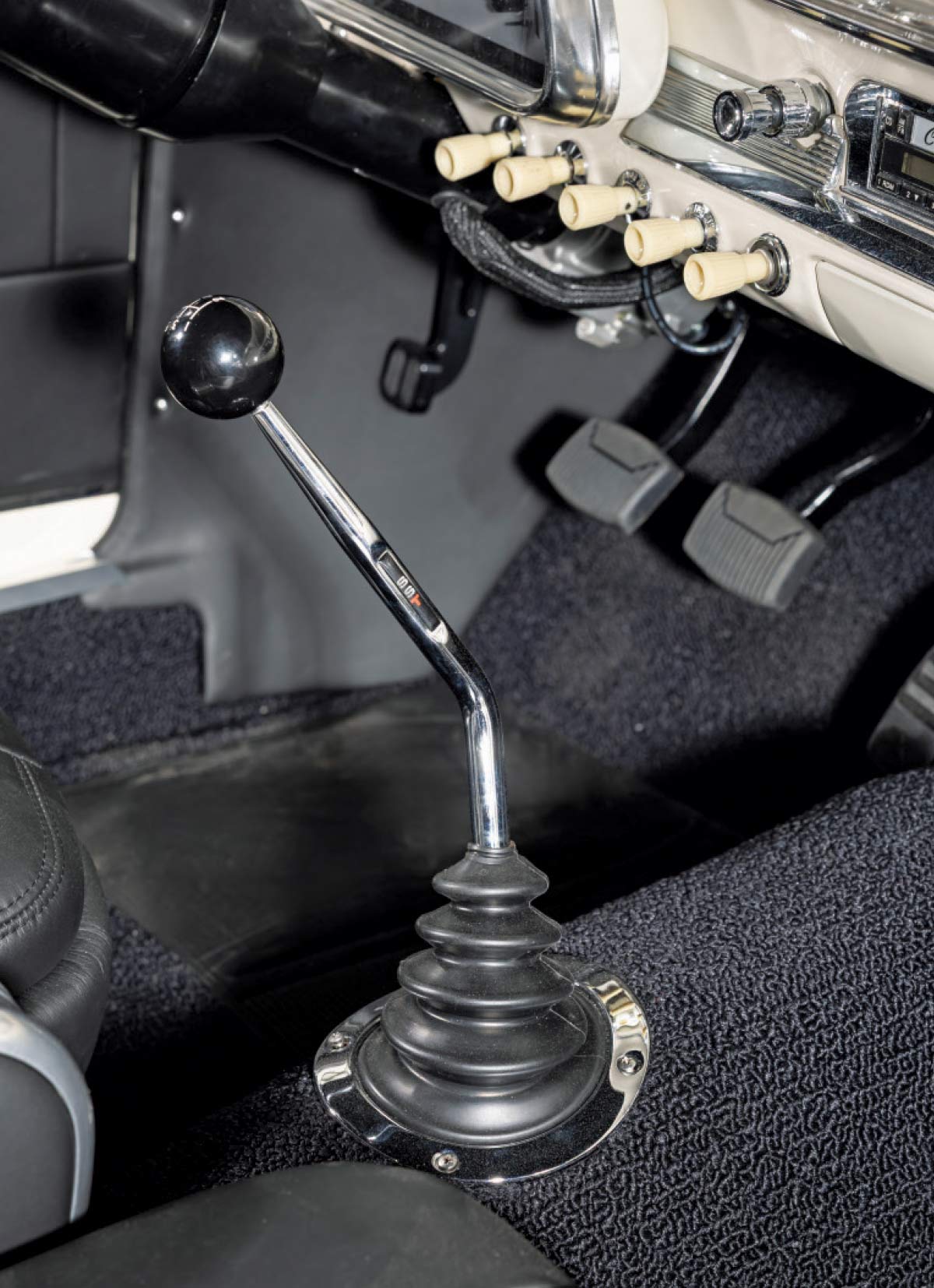 Close-up of a chrome manual gear shifter with a black knob and "SST" logo, mounted on black textured carpeting.