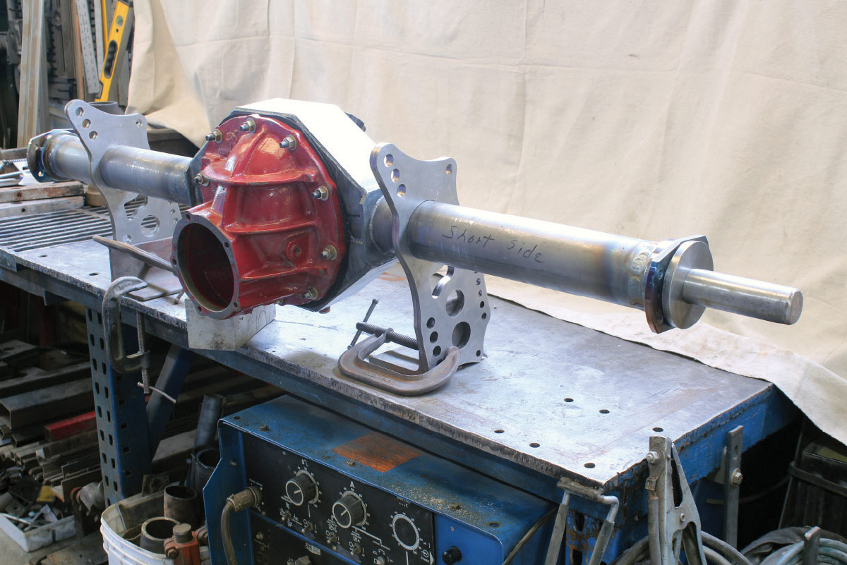 A red differential carrier assembled into a custom silver axle housing with metal brackets, clamped to a workbench.