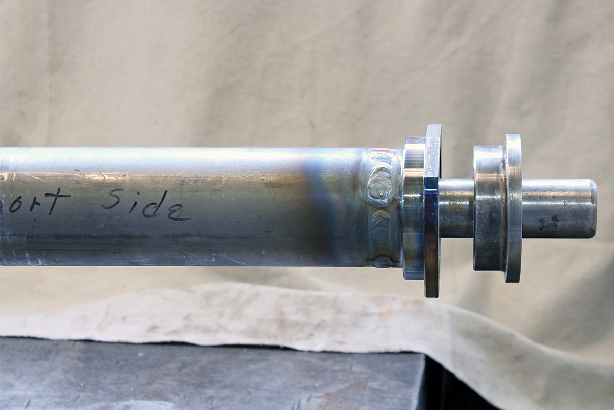 Close-up of a welded metal flange on a steel axle tube, showing heat discoloration and a precise circular weld.