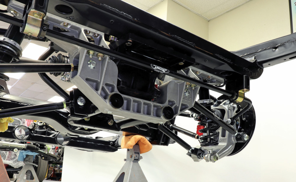Low-angle view of the Detroit Speed IRS cradle assembly installed on a black powder-coated C3 Corvette chassis. The assembly features a silver aluminum lower section and a black steel upper section, shown mounted with coilovers and sway bars.