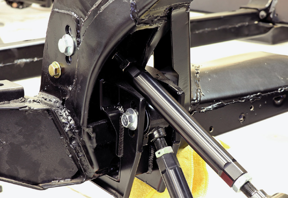 Close-up of the rear chassis with the Detroit Speed IRS installation, showing black upper and lower trailing links secured with silver bolts to a heavy-duty steel bracket welded into the frame kick-up.
