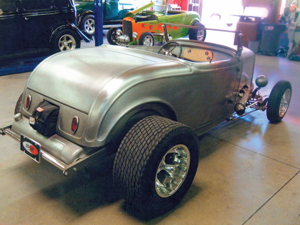 A bare metal 1932 Ford roadster in the SO-CAL Speed Shop. The rear view shows large tires, a parachute, and a mocked-up dash. In the background, the green and orange flamed "Limefire" roadster is parked in the garage.