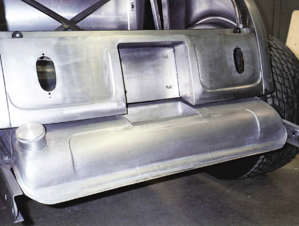 Close-up of the bare metal roadster's rear bodywork, featuring a custom-fabricated recessed channel for a parachute mount that spans the center of the rear panel and the top of the fuel tank.