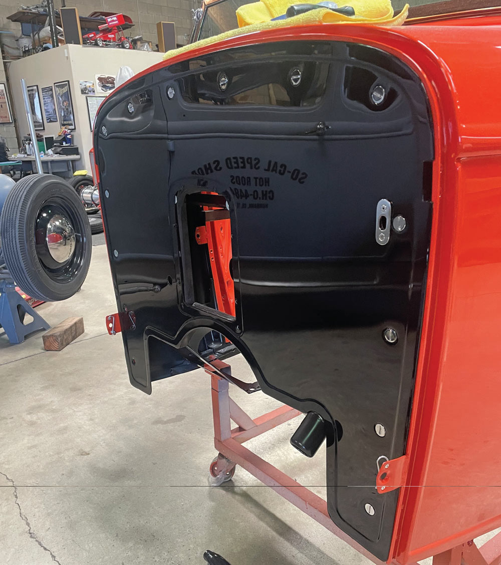 Close-up of the red roadster body featuring a newly installed gloss black outer firewall. The firewall includes a rectangular center opening for distributor access and clearly reflects the SO-CAL Speed Shop logo in its polished surface.