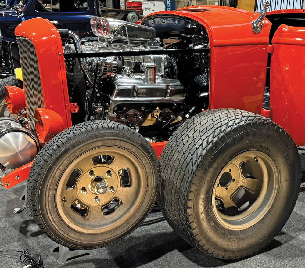 Two magnesium Halibrand Sprint wheels with Michelin and Firestone tires lean against the front of the finished red roadster. The supercharged engine and polished chrome components are visible in the background.