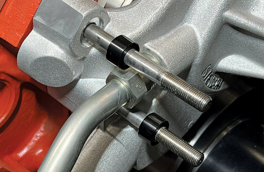 Close-up of black spacer bushings installed on mounting studs between a silver Stewart water pump and an orange engine block for a Front Runner accessory drive system