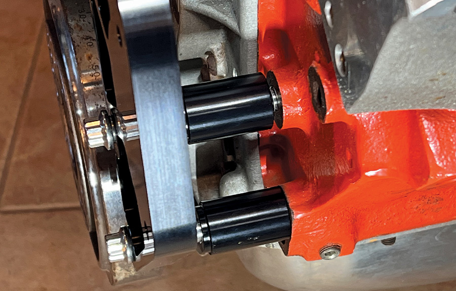 Close-up of black anodized spacers and mounting hardware securing a CNC-machined bracket to an orange Chevrolet V8 engine block for a Front Runner accessory drive system