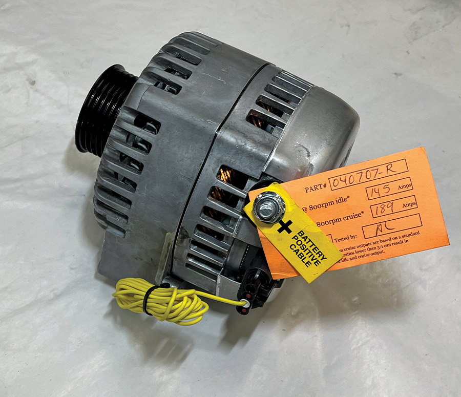 A high-output performance alternator for a Front Runner engine drive system, featuring a raw aluminum housing, a black serpentine pulley, and a testing tag showing 145 amps at idle