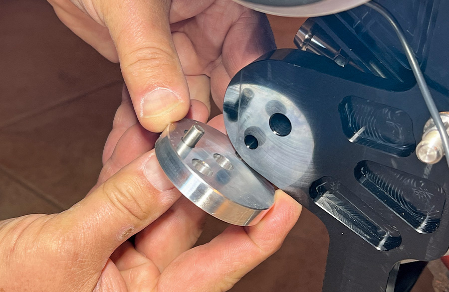 A close-up of a mechanic aligning a silver aluminum pulley hub with a black anodized engine bracket, showing the critical placement of the steel dowel pin for proper component clocking