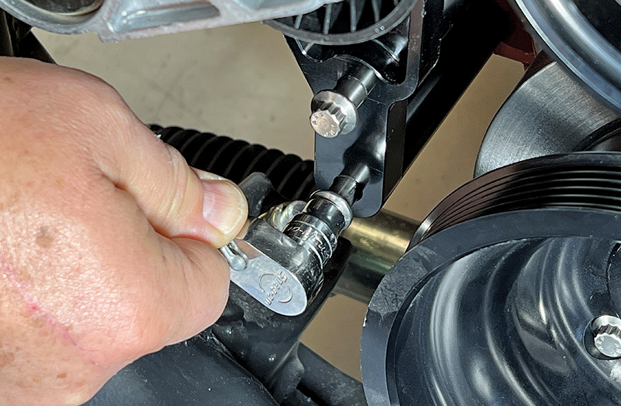 A close-up action shot of a mechanic using a silver ratchet and socket to tighten the mounting bolts on a black anodized engine bracket for a Front Runner serpentine drive system