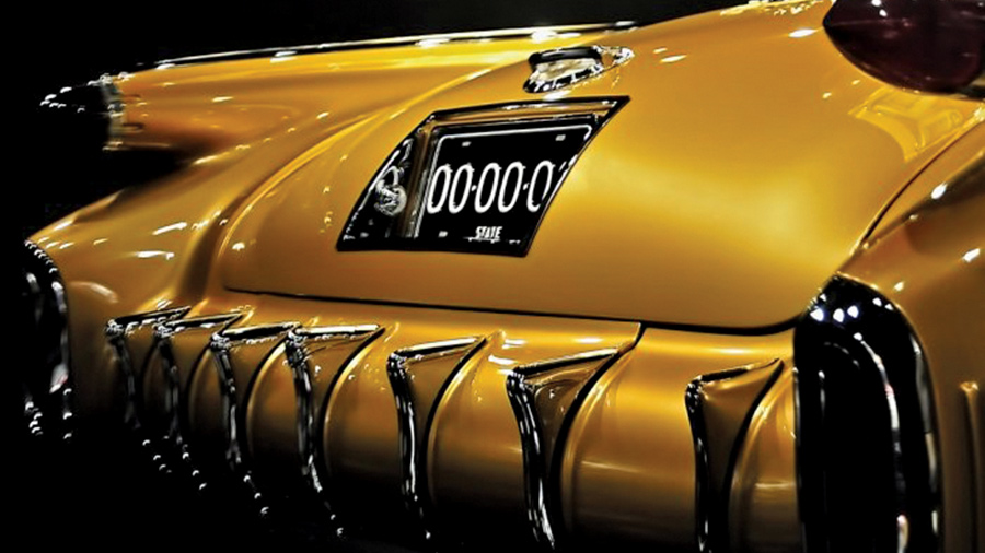 A close-up of the rear deck and bumper of the gold 1954 Oldsmobile F-88 concept car, highlighting the vertical chrome bumper guards and the integrated license plate housing