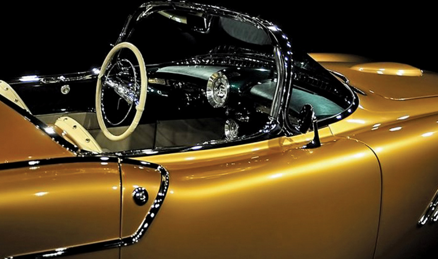 A side-view close-up of the 1954 Oldsmobile F-88 concept car's interior, featuring a metallic gold exterior, a thin-rimmed white steering wheel, and a dramatic wrap-around windshield
