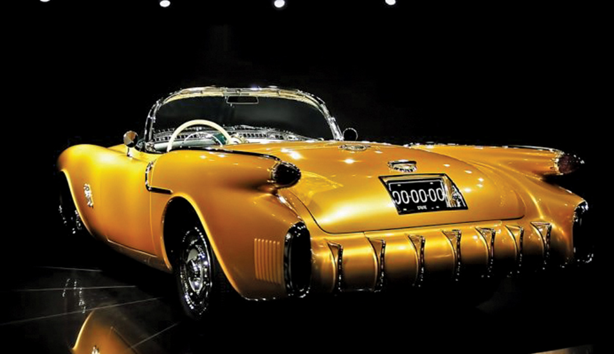 A rear three-quarter studio shot of the 1954 Oldsmobile F-88 concept car in metallic gold, showcasing its unique "rocket" taillights, integrated rear bumper with chrome vertical guards, and wrap-around windshield
