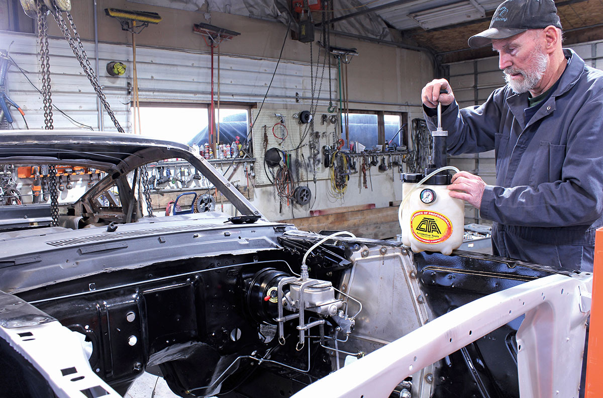Mechanic using a pressure bleeder on a Mustang master cylinder.