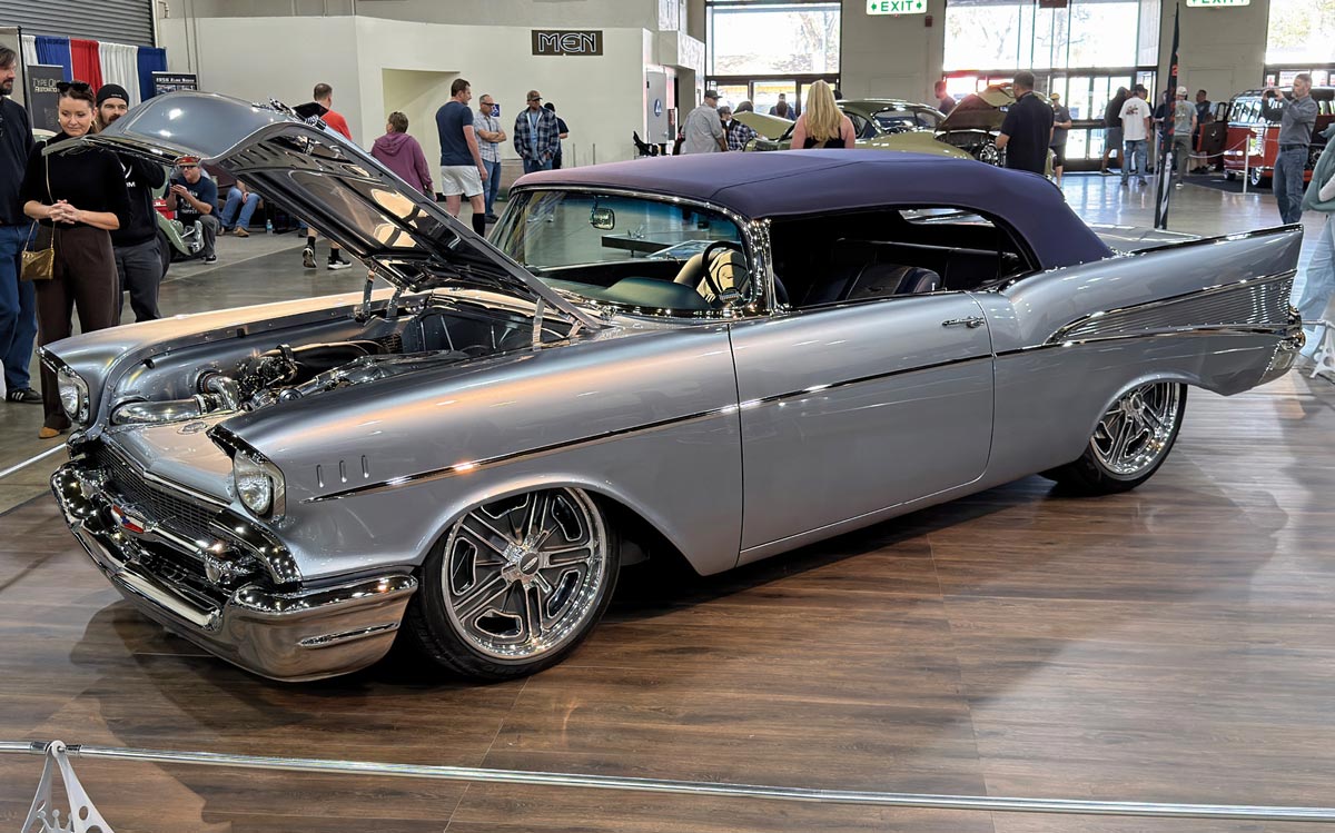 1957 Chevrolet Bel Air Silver two-door coupe with hood open, showcasing custom purple interior and polished chrome details at an indoor car show