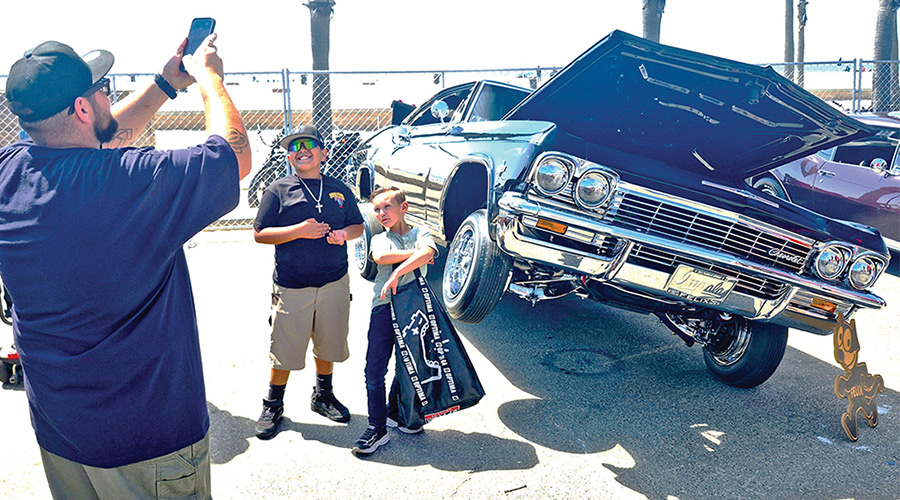 Family photographing a black 1965 Chevrolet Impala lowrider