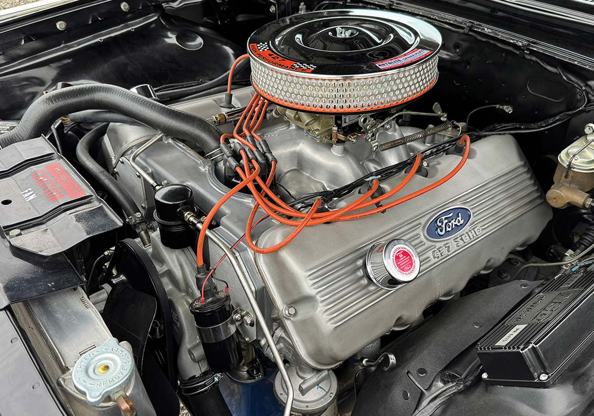 A clean engine bay showcasing a Ford 427 SOHC engine with silver finned valve covers, bright orange spark plug wires, and a round chrome high-performance air cleaner.