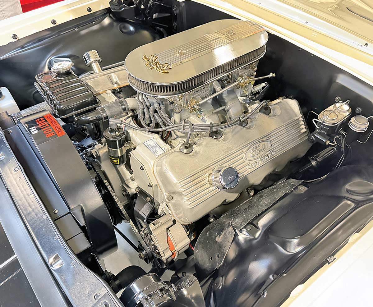 A clean car engine bay showcasing a Ford 427 SOHC engine with silver finned valve covers and a large, oval-shaped polished chrome air cleaner on top.