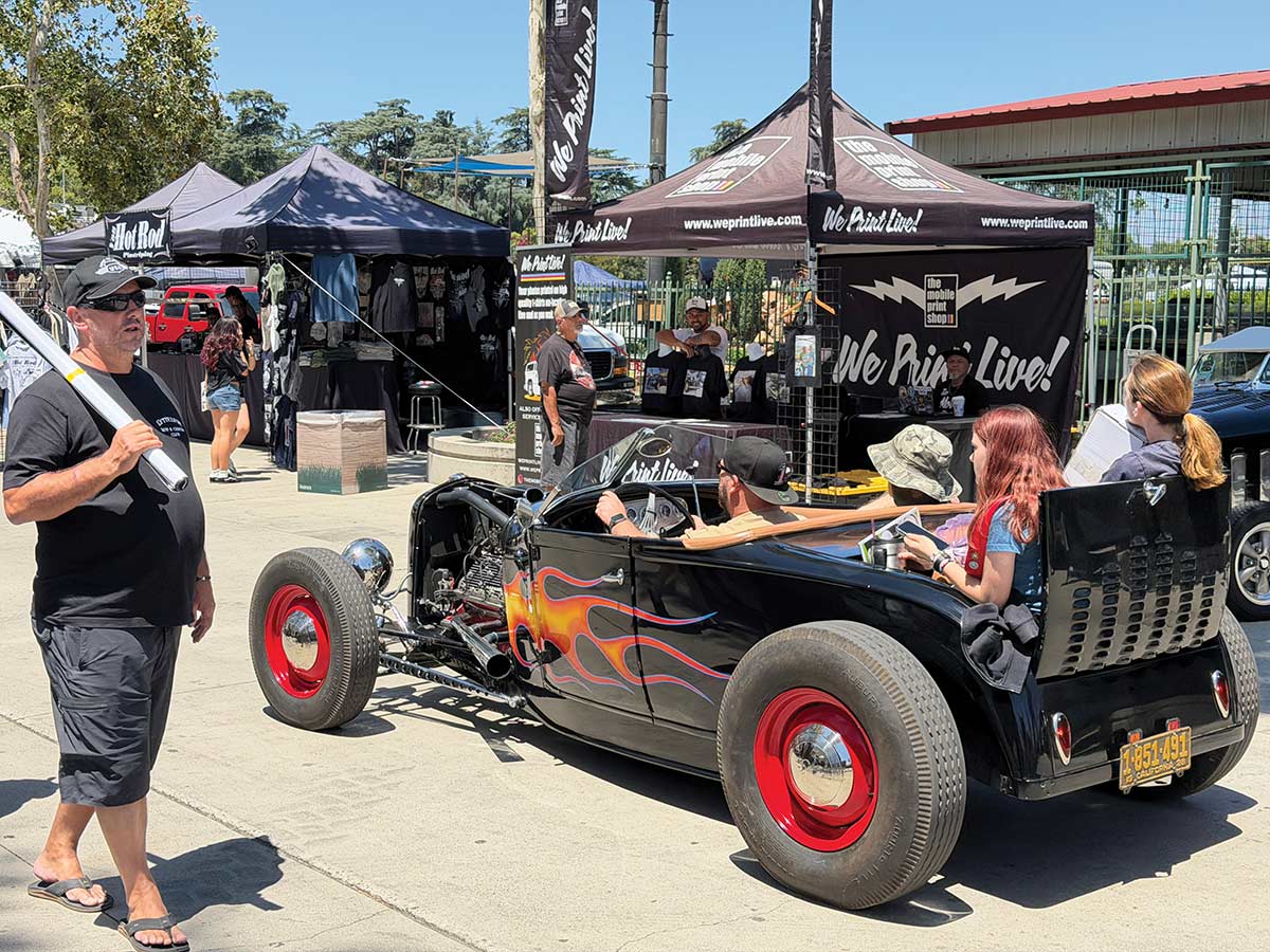 Black flamed 1932 Ford roadster with passengers parked at an outdoor car show.