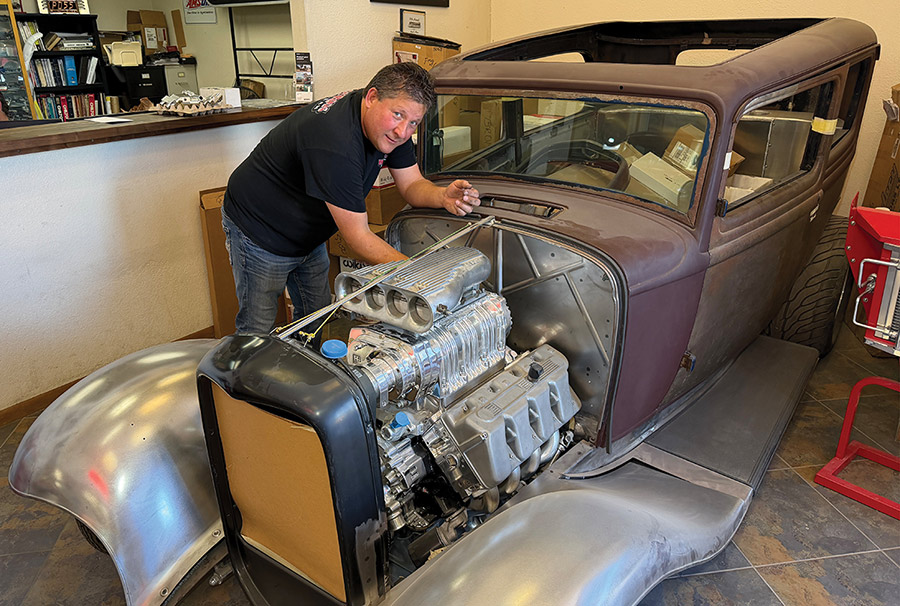 Man standing over a supercharged Boss 429 engine in a 1932 Ford project.