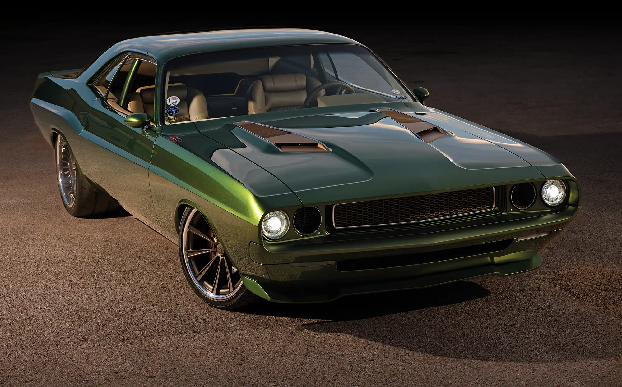 A custom metallic green classic Dodge Challenger muscle car parked on asphalt, featuring modern aftermarket wheels, hood scoops, and illuminated headlights.