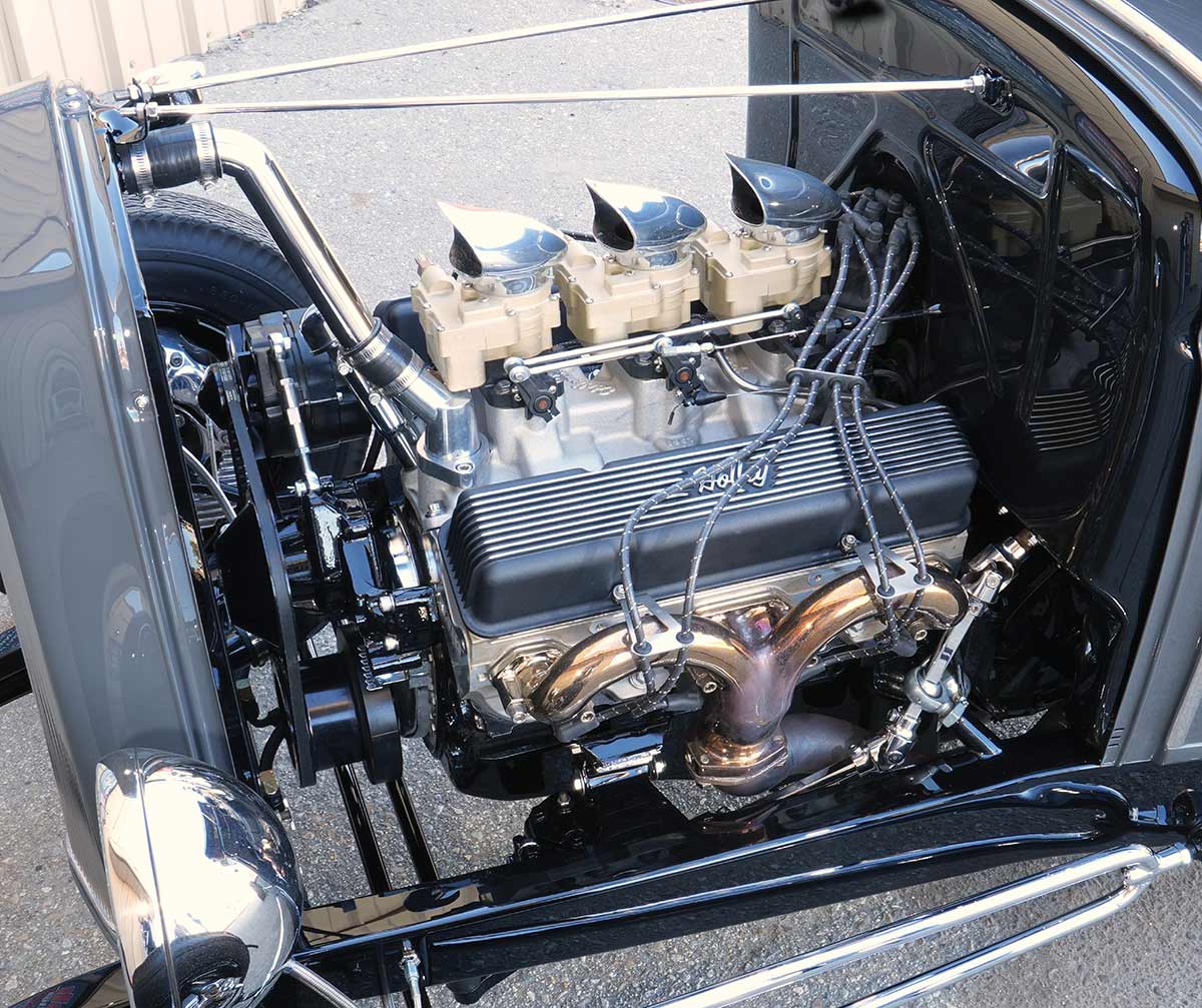 Detailed view of a classic hot rod engine bay featuring a V8 engine equipped with a tri-power triple carburetor setup and chrome scoop air cleaners.